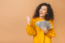Portrait Of A Cheerful Young Woman Holding Money Banknotes And Celebrating Isolated Over Beige Background.