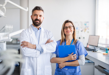 Wall Mural - Dentist with dental assistant in modern dental surgery, looking at camera.