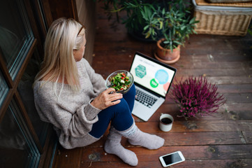 Wall Mural - Senior woman with laptop sitting outdoors on terrace, working.