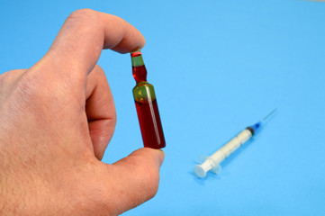 Ampoule with vaccine from a new coronavirus in a human hand on a blue background, flu vaccination concept