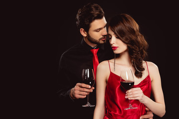 Wall Mural - Elegant man embracing beautiful girlfriend with glass of red wine isolated on black