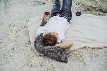 A young man on nature at the edge of the earth uses a smartphone. Lake, mountains. Weekend in nature with a gadget. Harmony with nature and technology.