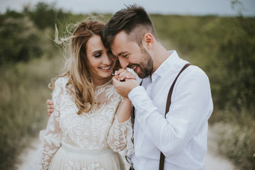 Smiling bride and groom spending time together. Posing on the mountain hills background. Dressed in white dress beautiful blonde caucasian bride and handsome groom. Hugs, kissess and enjoy the company