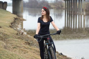 Girl on a mountain bike on offroad, beautiful portrait of a cyclist in rainy weather, Fitness girl rides a modern carbon fiber mountain bike in sportswear. Close-up portrait of a girl in red bandana.