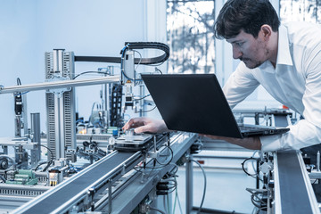 Industry 4.0 concept; Engineer is working on laptop to program smart factory prototype's automation. automated car on production line,  artificial intelligence in smart manufacturing.