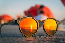 Pair Of Sunglasses On The Beach With The Reflection Of The Sunset