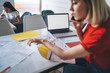 © BullRun - Multitask woman speaking on smartphone checking documents at table with laptop