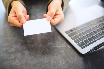 Top view image of a  businesswoman holding and giving a blank business cards while using laptop computer in office