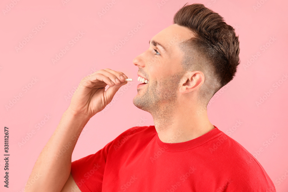 Handsome young man with chewing gum on color background