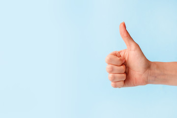 closeup of female hand showing thumbs up sign against pastel blue background, copy space, minimal co