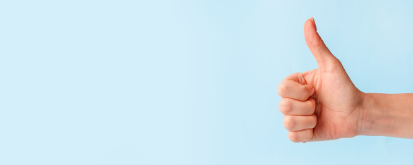 closeup of female hand showing thumbs up sign against pastel blue background, copy space, minimal co