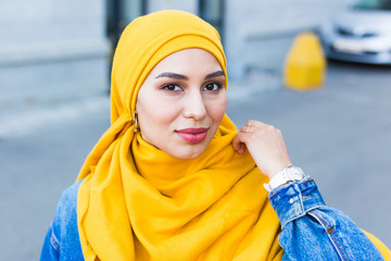 Wall Mural - Beautiful Arabic muslim woman wearing yellow hijab, stylish female face portrait over city street.