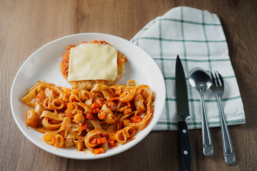 Pasta, Italian food, with tomato sauce topping with deep fried crispy pork cutlet and a sheet of cheese in white dish place on a cloth and on dark brown wooden table