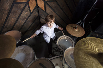 The boy learns to play the drums. The child behind the drum kit.