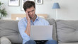 © stockbakers - Handsome Young Man with Headache Working on Laptop while Sitting on Couch
