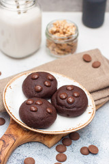 Chocolate cookies with choco drops on white plate, and glass of milk