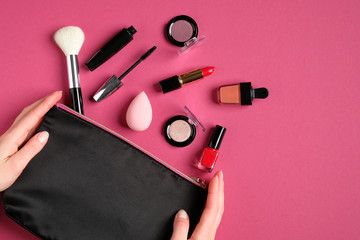 Wall Mural - Cosmetic pouch with professional decorative cosmetics and makeup tools in female hands over pink background. Top view, flat lay. Beauty and fashion concept.