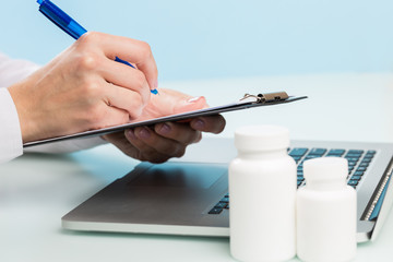 Doctor's hand uses a laptop and writes with a pen on paper on a blue background