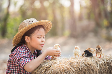 Poster - happy little girl with of small chickens sitting outdoor. portrait of an adorable little girl, preschool or school age, happy child holding a fluffy baby chicks with both hands and smiling..