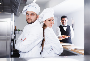 two chefs, standing back to back in kitchen