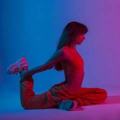 Wall Mural - Young beautiful woman in a sexy top in pants doing yoga in a studio with bright neon blue-violet light. Sporty girl in trendy wear doing stretching with a multi-colored color in the style disco.