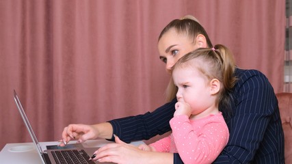 young beautiful blonde and her charming little daughter are shopping online with a laptop and credit card. Shopping in the online store.