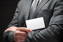 White Blank Business Card Closeup In Businessman Hand, Gray Suit, Dark Wall Background