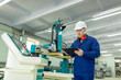 © Bogdan - CNC machine operator in the Hard  white Hat Walks Through Light Modern Factory While Holding tablet. Successful, Handsome Man in Modern Industrial Environment.
