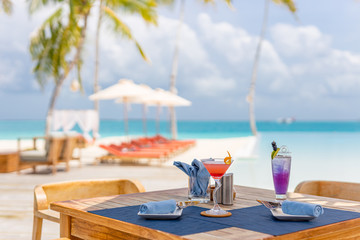 Two cocktails on luxury tropical vacation with blurred beach scenery, infinity swimming pool, loungers, deck chairs with umbrella