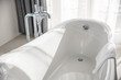 Bathtub in master bathroom in new luxury home, white tub, towel in soft sunlight. Elegant hotel or resort interior