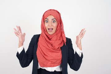 Wall Mural - Portrait of beautiful female looks with excitement at camera, keeps hands raised over head, notices something unexpected, isolated over gray wall. Lovely woman reacts on sudden news.