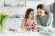 © LIGHTFIELD STUDIOS - Happy kid and mother painting easter eggs near tulips and decorative bunnies