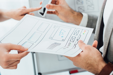 cropped view of ux developers using smartphone and template of website near whiteboard isolated on w