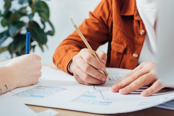 Cropped view of developers with pencil and marker working with project of user experience design at table