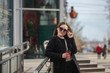 © Юлия Буракова - cheerful woman on a city street drinks coffee on a sunny day and looks at the camera. coffee to go. Portrait of a girl with a drink in hands