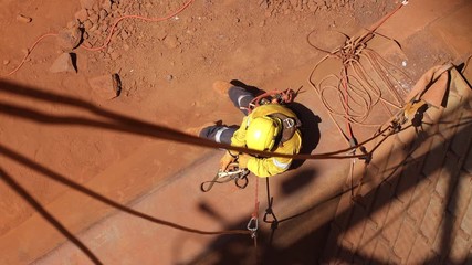 Wall Mural - Safe work practices topeview 4K high quality footage of rope access welder worker wearing full safety harness equipment disconnecting secondary safety backup device in the safe manner Australia   