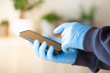 man hands in gloves using smartphone, preventing germs coronavirus bacteria