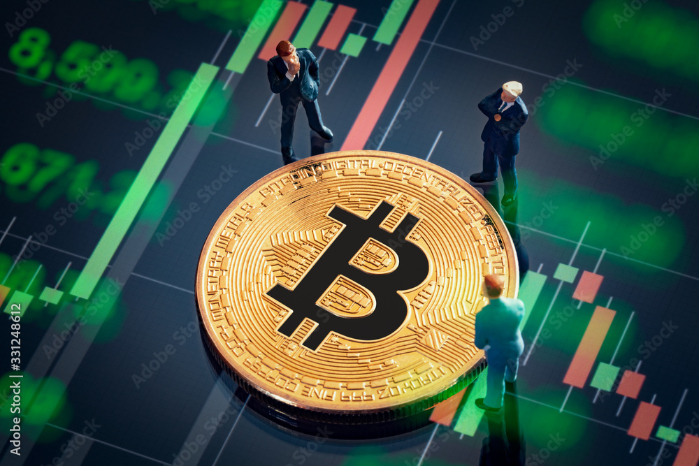 Business meeting about the investment decision for bitcoin concept: Macro miniature businessman figurines standing near the shiny golden bitcoin. Colorful stock market graphic chart on background.