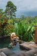 Girl in a private pool in Bali admires a beautiful view of the palm trees. Luxury holiday. Woman resting in the pool with a beautiful view of the palm trees on the island of Bali