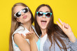 Young happy girlfriends in sunglasses sending air kiss on yellow background