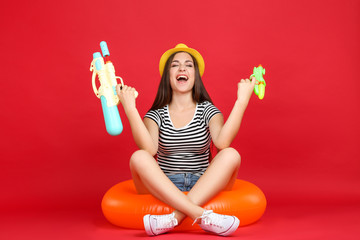 Young girl with inflatable ring and water guns on red background