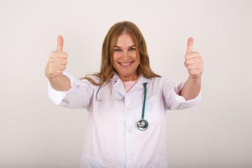 Good job! Portrait of a happy smiling doctor young successful woman giving two thumbs up gesture standing indoors. Positive human emotion facial expression body language. Funny girl