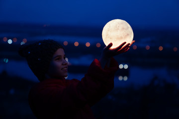 teenager girl in cap and jacket holds a full moon
