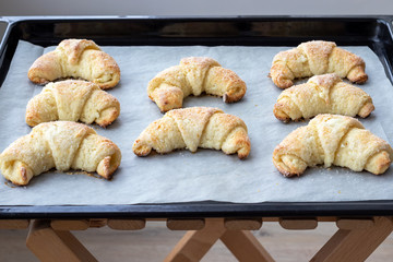 Baked croissants from a cottage cheese dough with sugar on a baking sheet on a wooden stool just taken out of the oven. Tea snack for breakfast. The process of making curd bagels or croissants