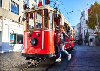 Wall Mural - Beautiful young girl tourist in a hat poses in front of tram at popular Istiklal street in Beyoglu, Istanbul, Turkey