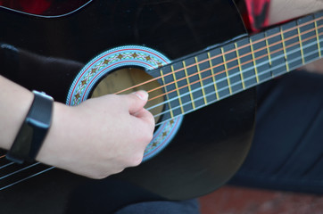 The neck of a classic black guitar. The girl's fingers pluck the strings. Songs with a guitar in the yard. Selective focus, close-up, background blur.