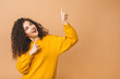 © denis_vermenko - Image of beautiful cute curly young woman standing isolated over beige background pointing up. Looking aside.