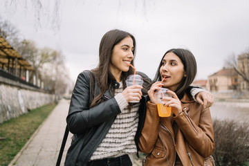 Sisters drinking fresh while walking on street