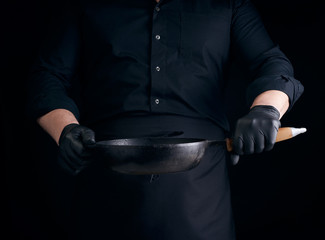 Wall Mural - male cook in black uniform and latex gloves holds an empty round vintage black cast iron pan