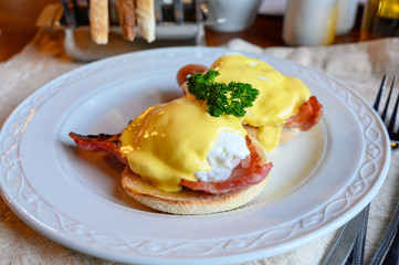 Weekend brunch in Scotland with two eggs benedict on homemade muffuns with roasted bacon and yellow hollandaise sauce.